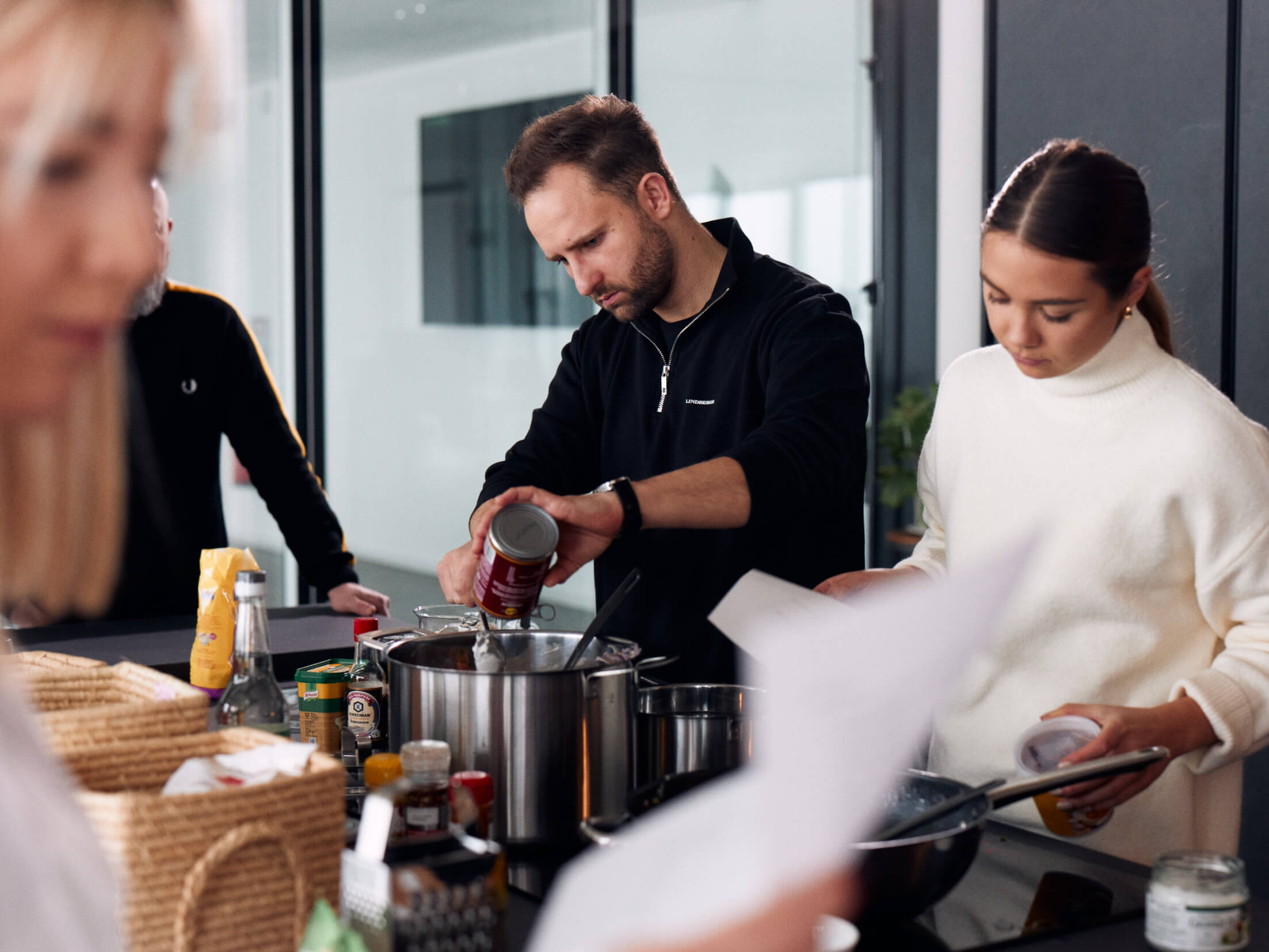 Zwei Mitarbeitende in der Agenturküche am Kochen. Im Vordergrund ist eine weitere Person unscharf zu sehen.