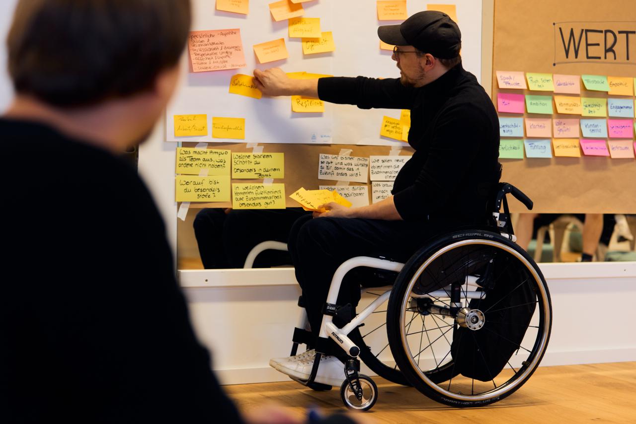 Workshop-Situation: Person im Rollstuhl klebt Zettel an die Wand.